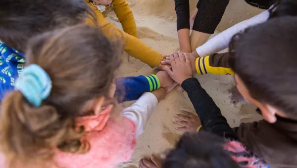 Children puts their hands into the middle of their circle as they play a game in a child-friendly space in Iraq.