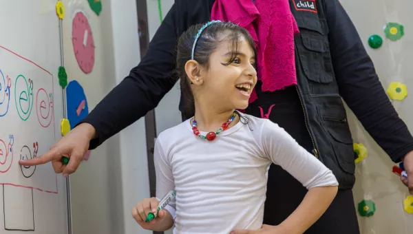 Girl smiles to her classmates as she completes a task on the whiteboard with the help of a War Child Education Facilitator in Jordan.