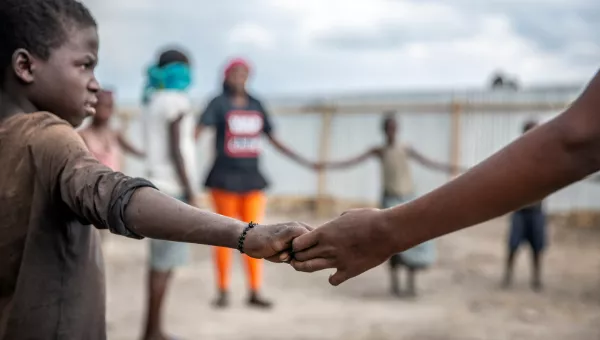 Children stand in a circle holding hands as they play games at a War Child child-friendly space in the DRC.