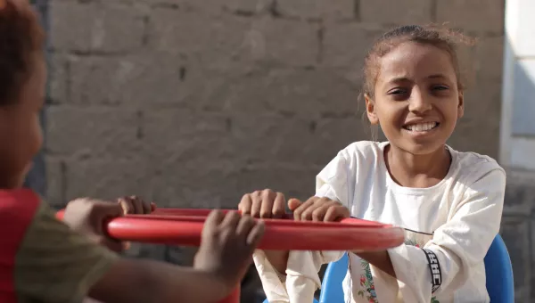 Little girl in Yemen plays on equipment outside a child-friendly space.