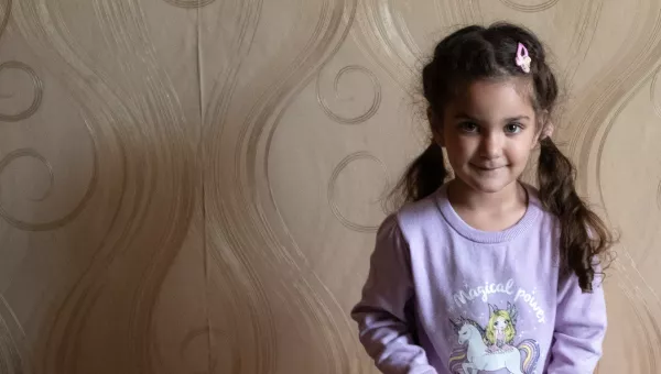 Girl in purple unicorn top standing against a wall in her home