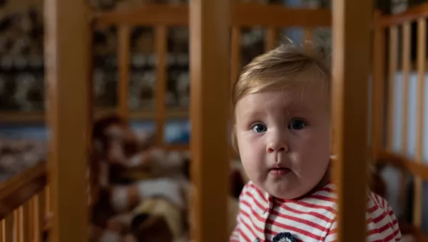 Ukrainian baby sits in cot looking at camera