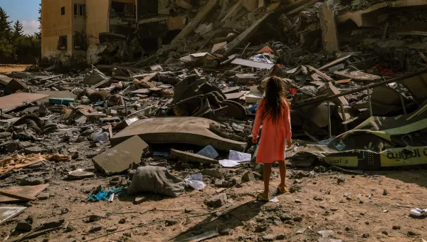 A girl standing in front of a collapsed building in Gaza. 