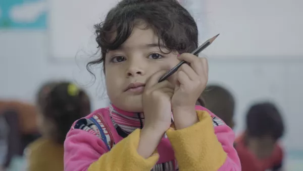 A girl in a classroom holding a pencil.