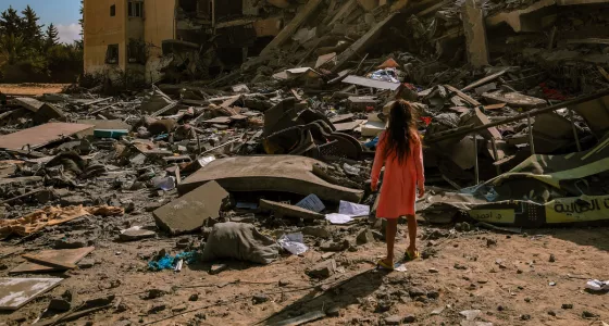 A girl standing in front of a collapsed building in Gaza. 