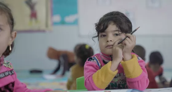 A girl sitting in a classroom holding a pencil.