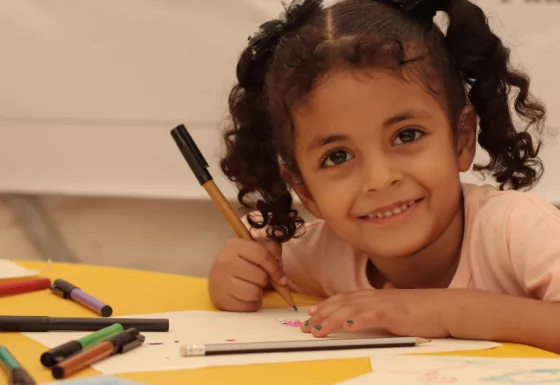 Yemeni girl smiles to the camera whilst colouring and drawing in a War Child child-friendly space in Yemen.